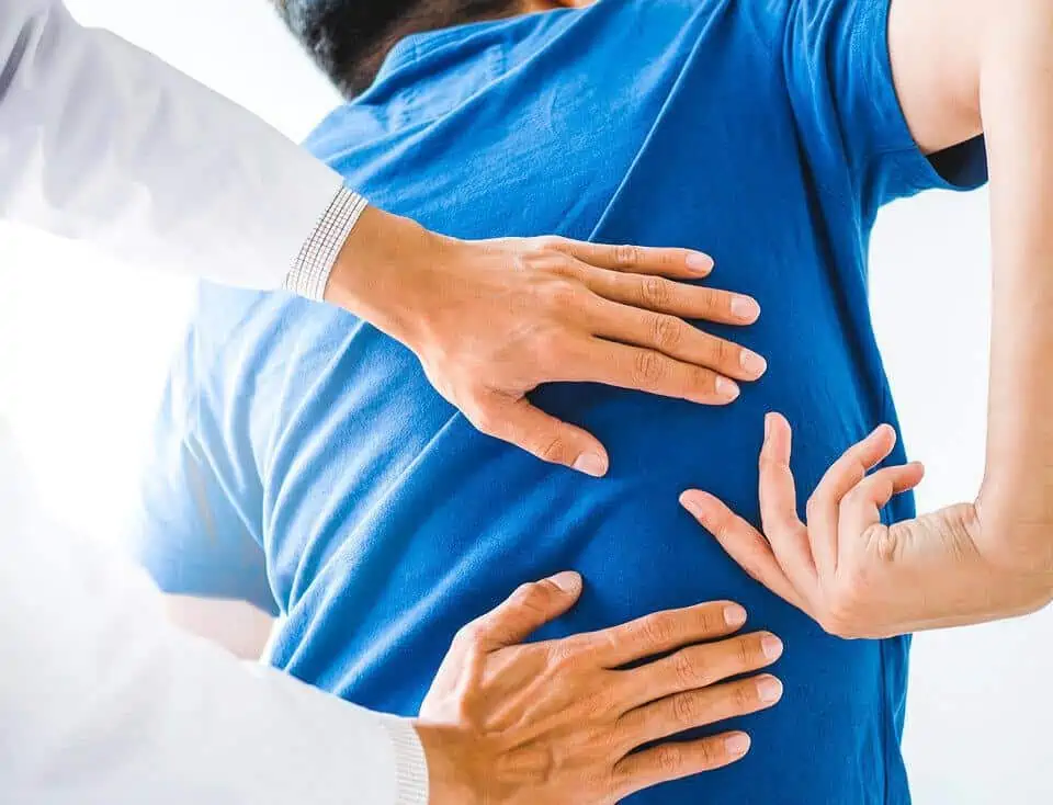 Image of a client pointing to the area of their back pain symptoms while a doctor palpates the area.