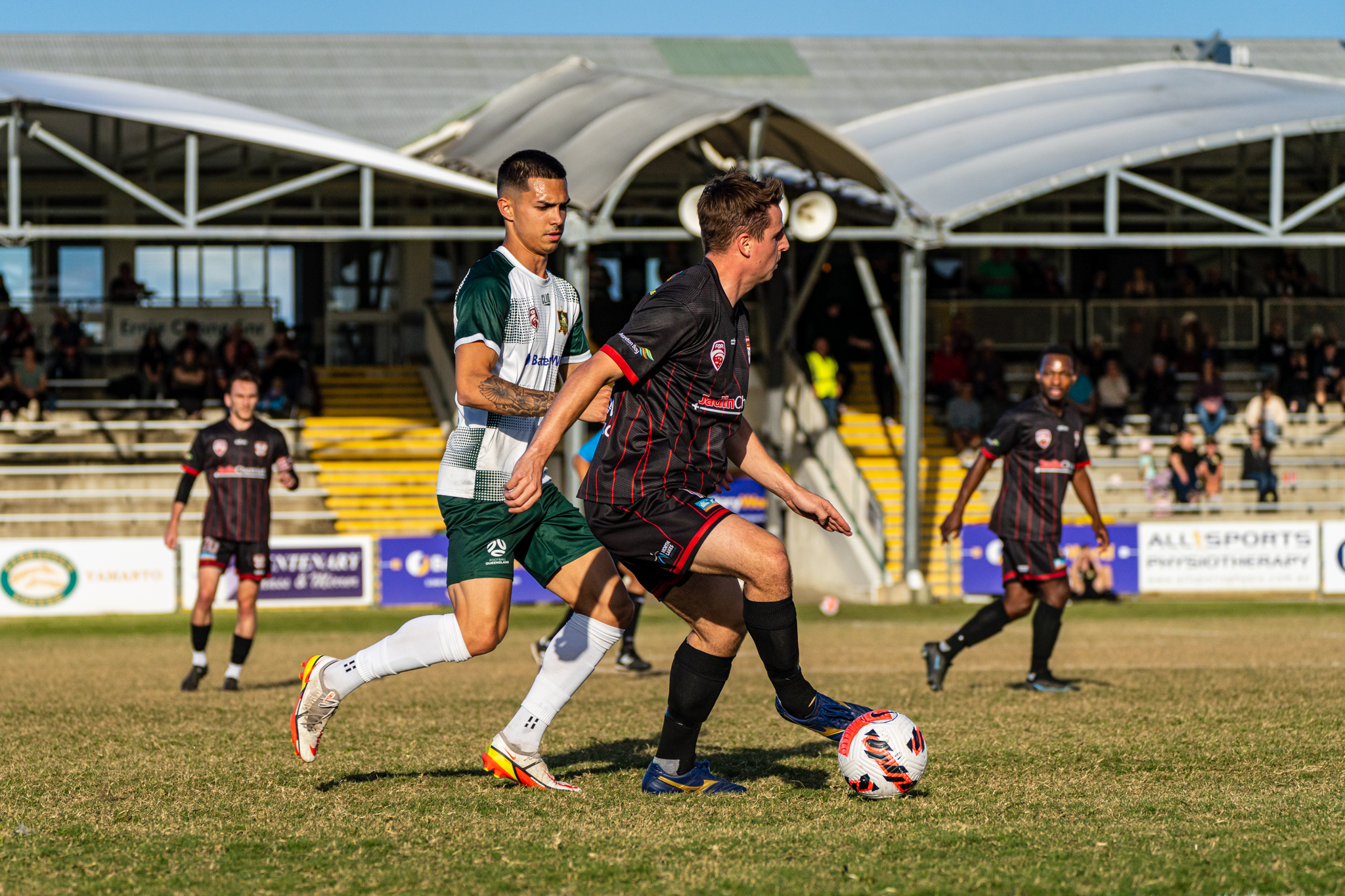 Footballers competing for the ball in front of a grandstand
