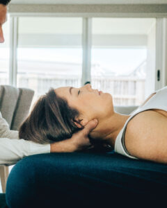 Physiotherapist treating a woman's neck as she lies on a treatment table at home
