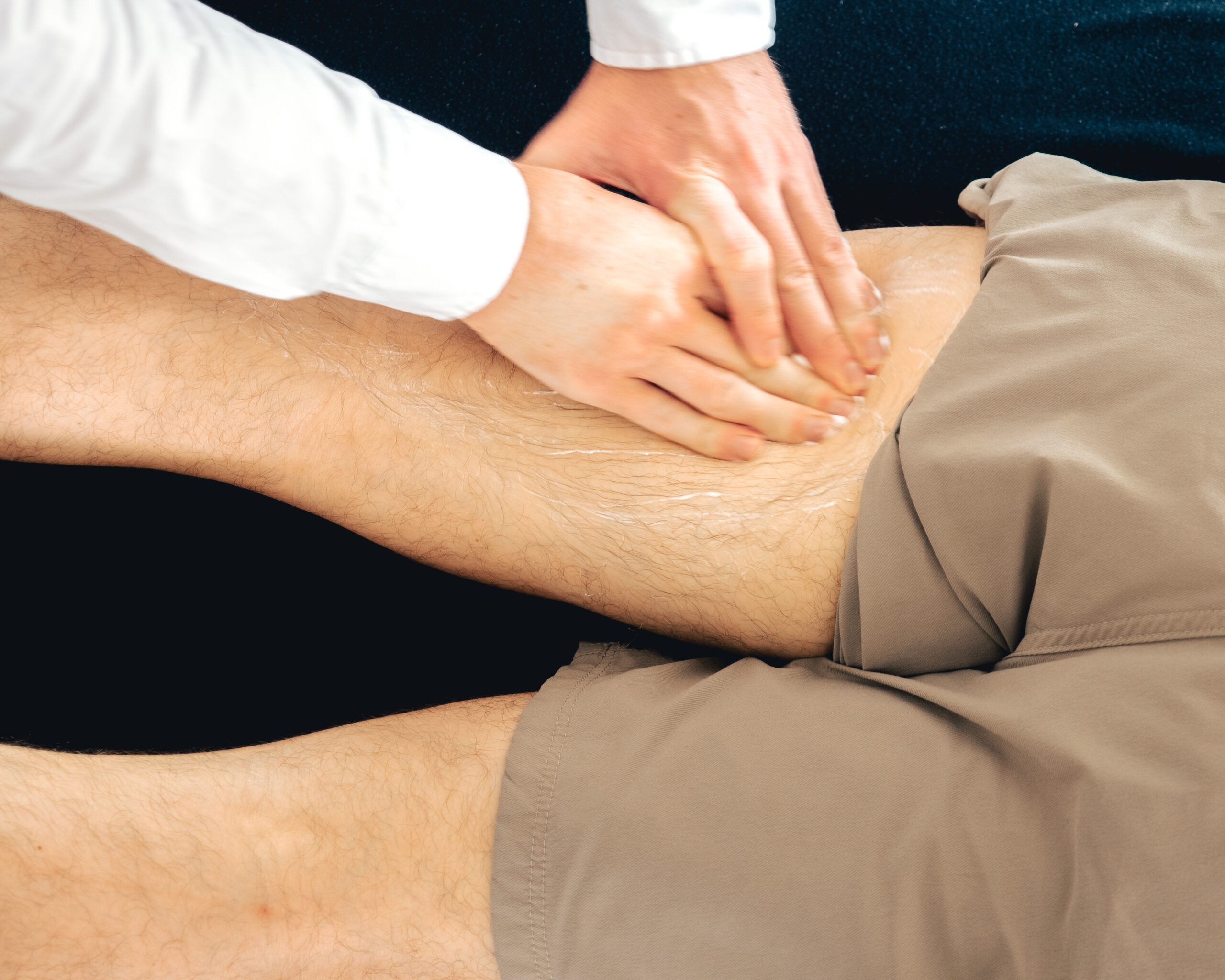 A man is receiving a sports massage on his leg from a sports physiotherapist.